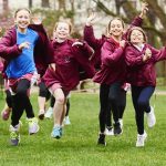 A group of 4 girls running across a field in their sports gear