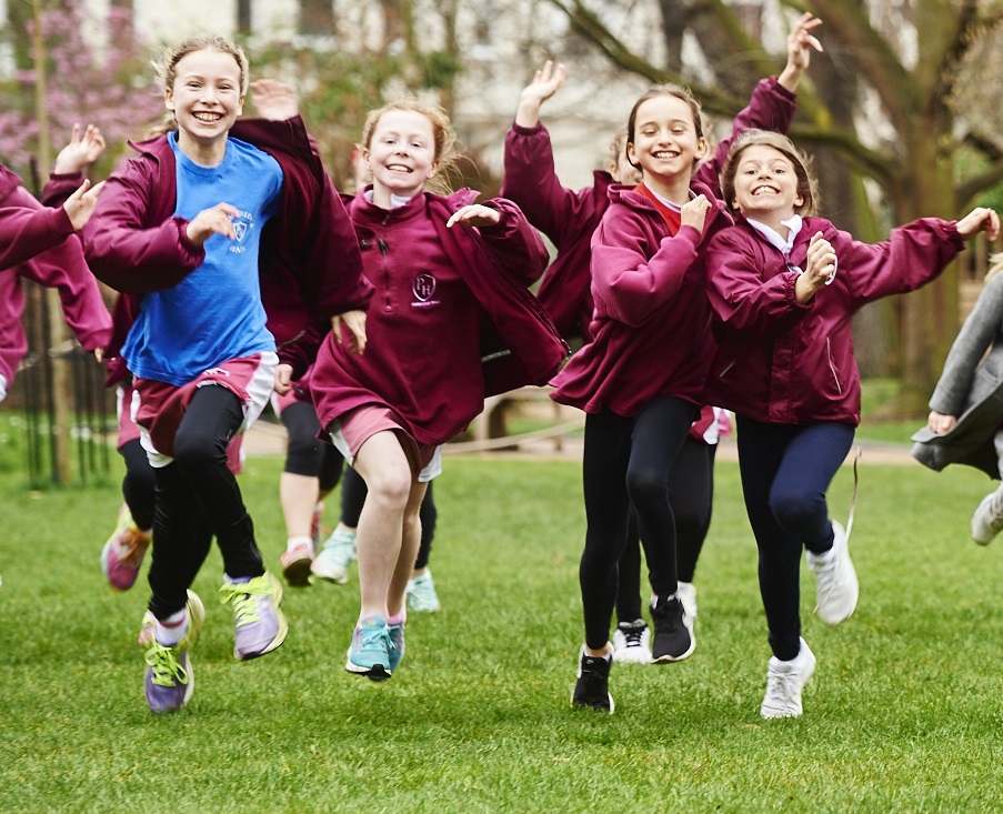 A group of 4 girls running across a field in their sports gear